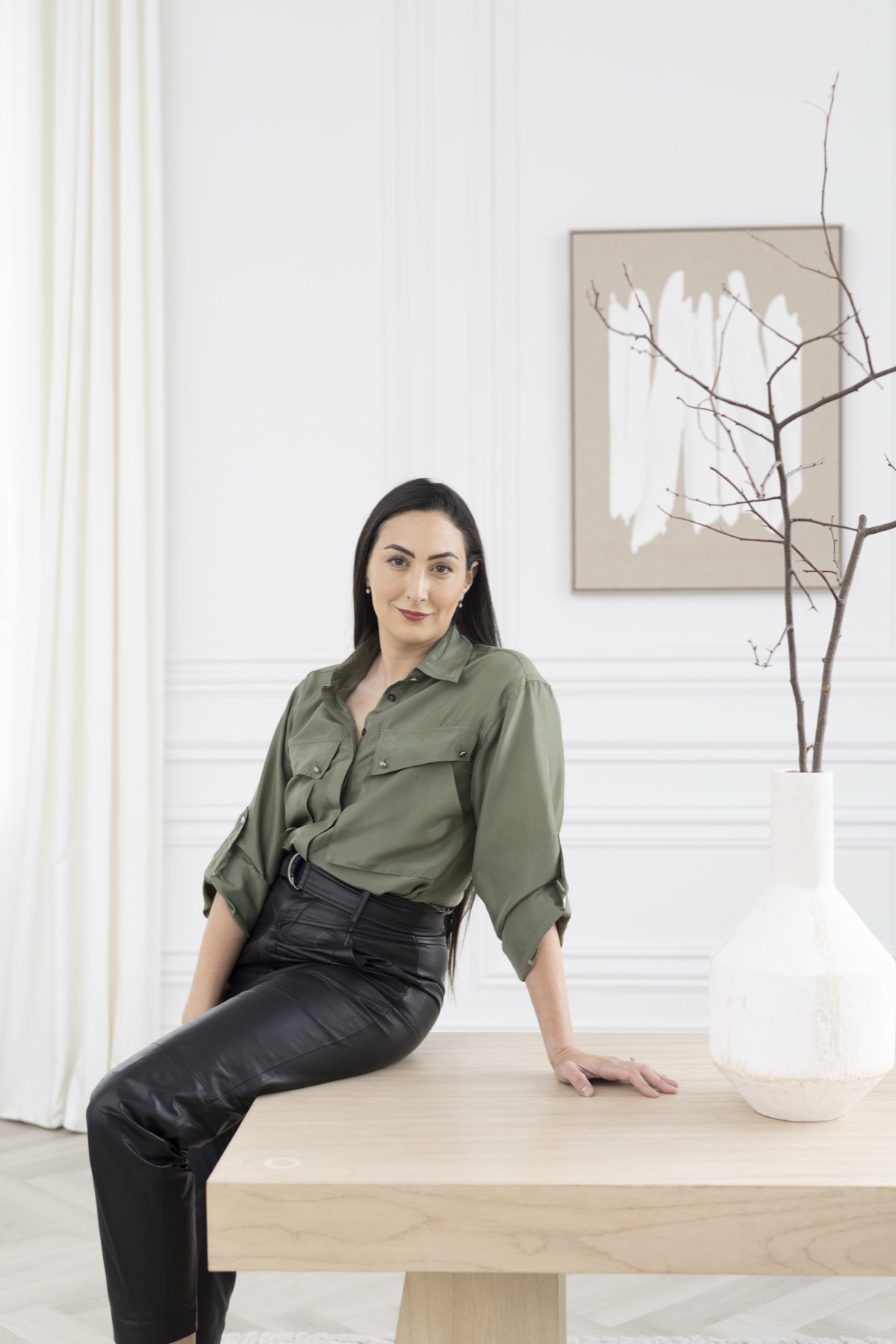 Rebecca Himelfarb seated on a pale oak bench in a bright white room